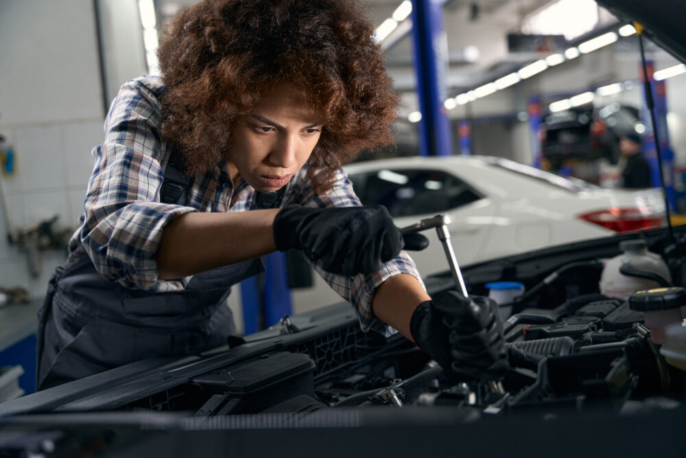Frau steht vor einer offenen Motorhaube und repariert ein Leasingfahrzeug